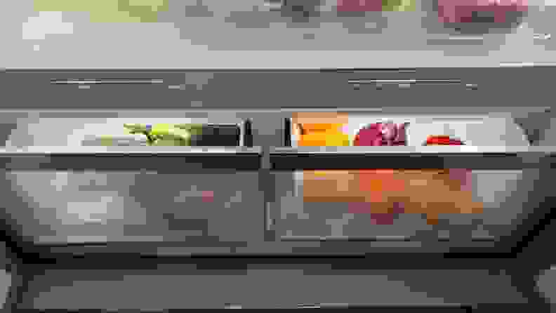 Open crisper drawers in a Bosch refrigerator full of oranges, peppers, and broccoli.
